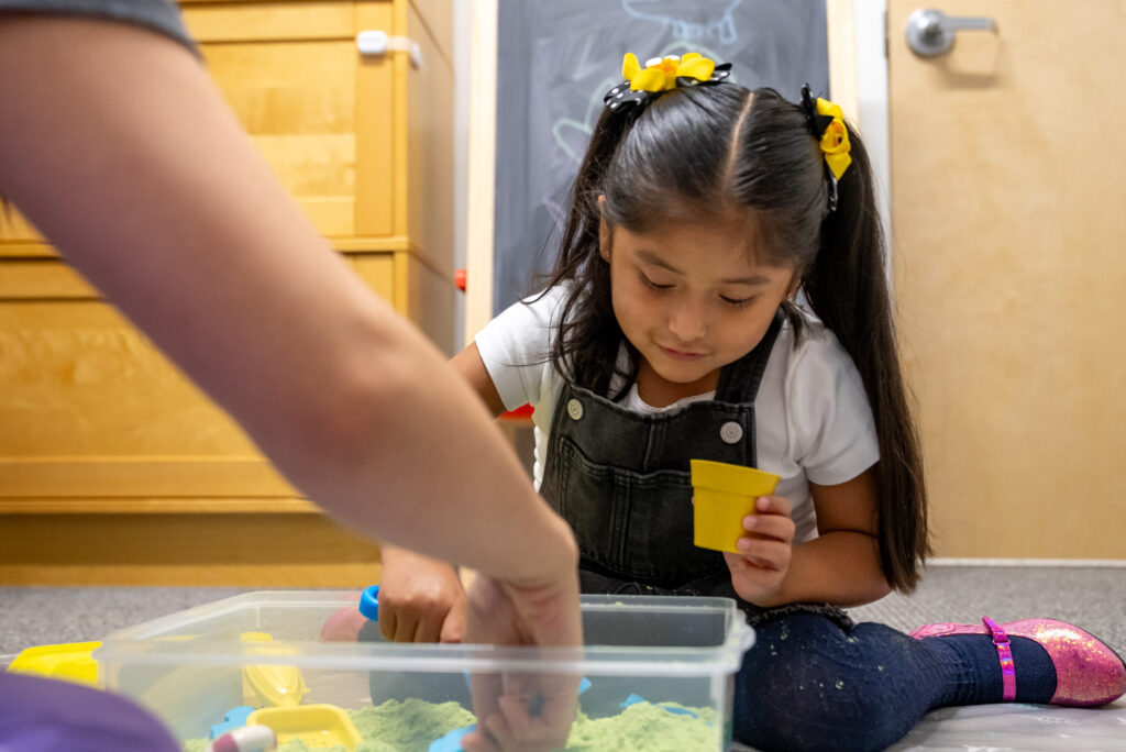 Young girl playing in a sensory bin with a therapist