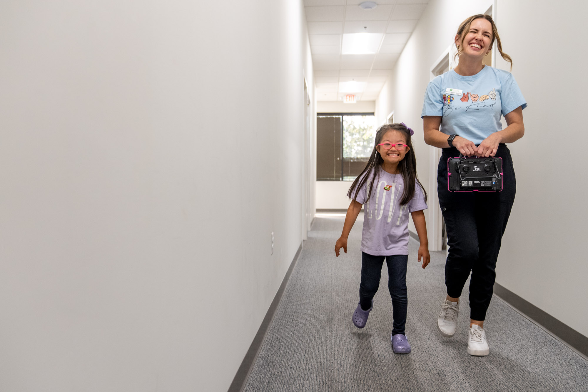 Therapist and young girl smiling as they walk down a hallway