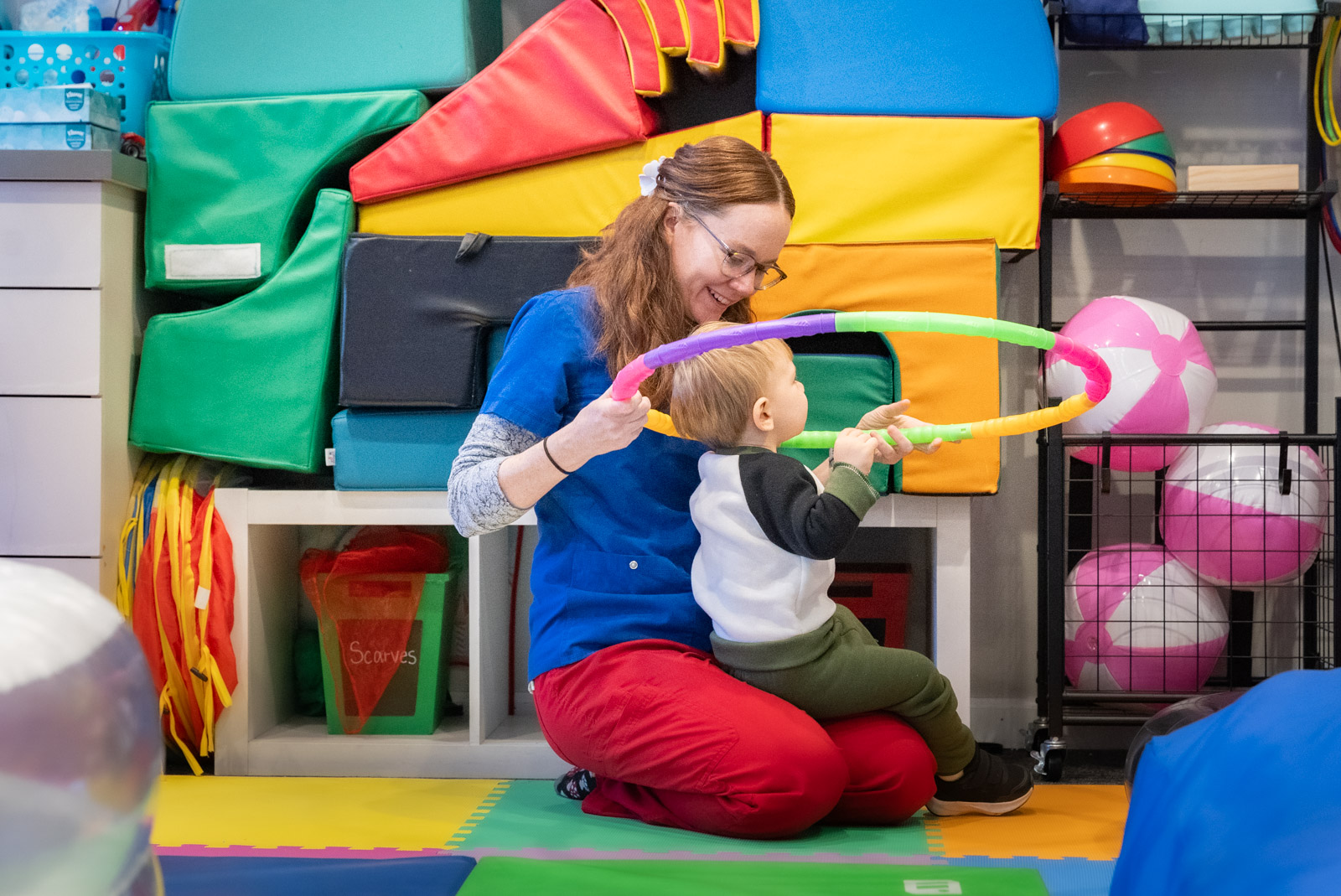 Therapist holding a hoop with a toddler in a colorful sensory gym
