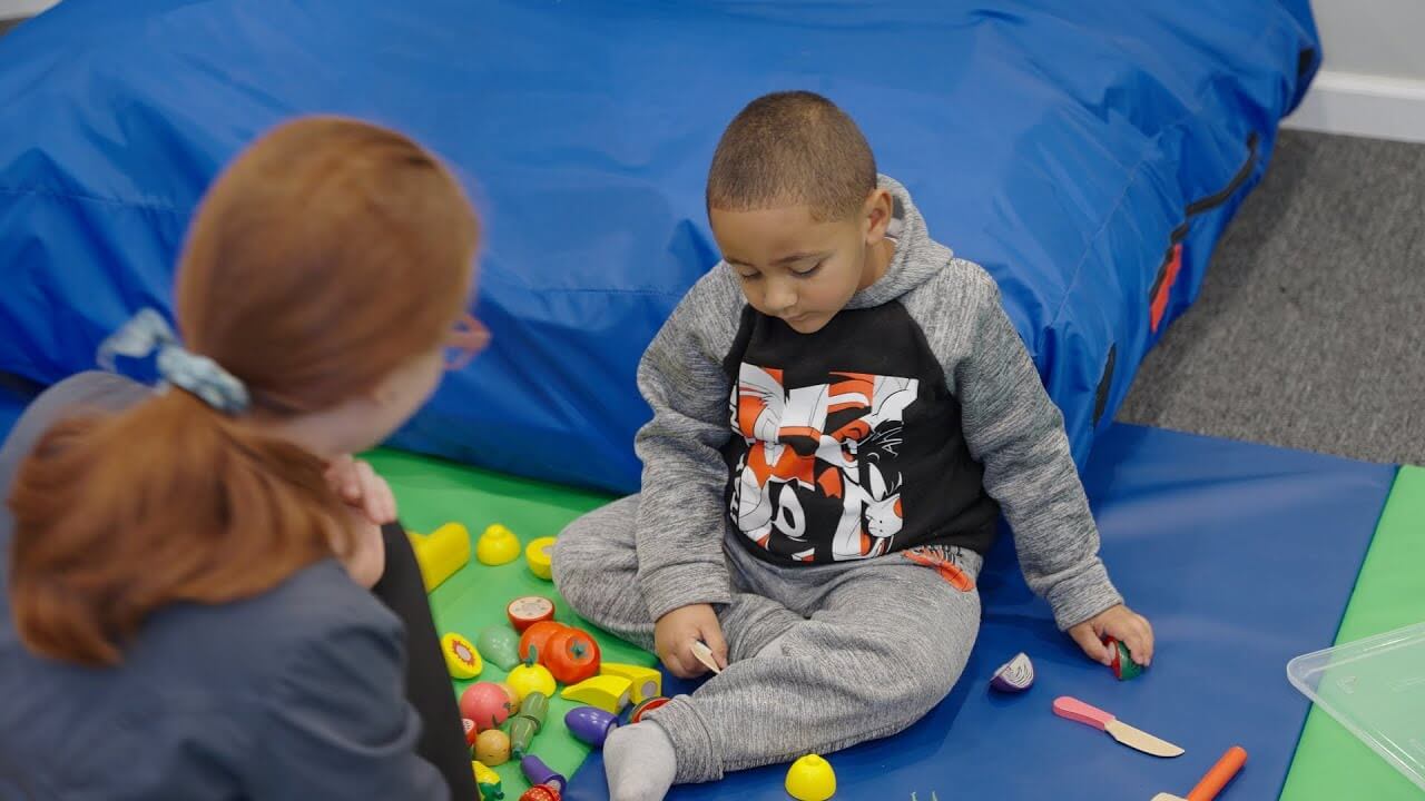 Therapist and young boy playing with toys on a mat