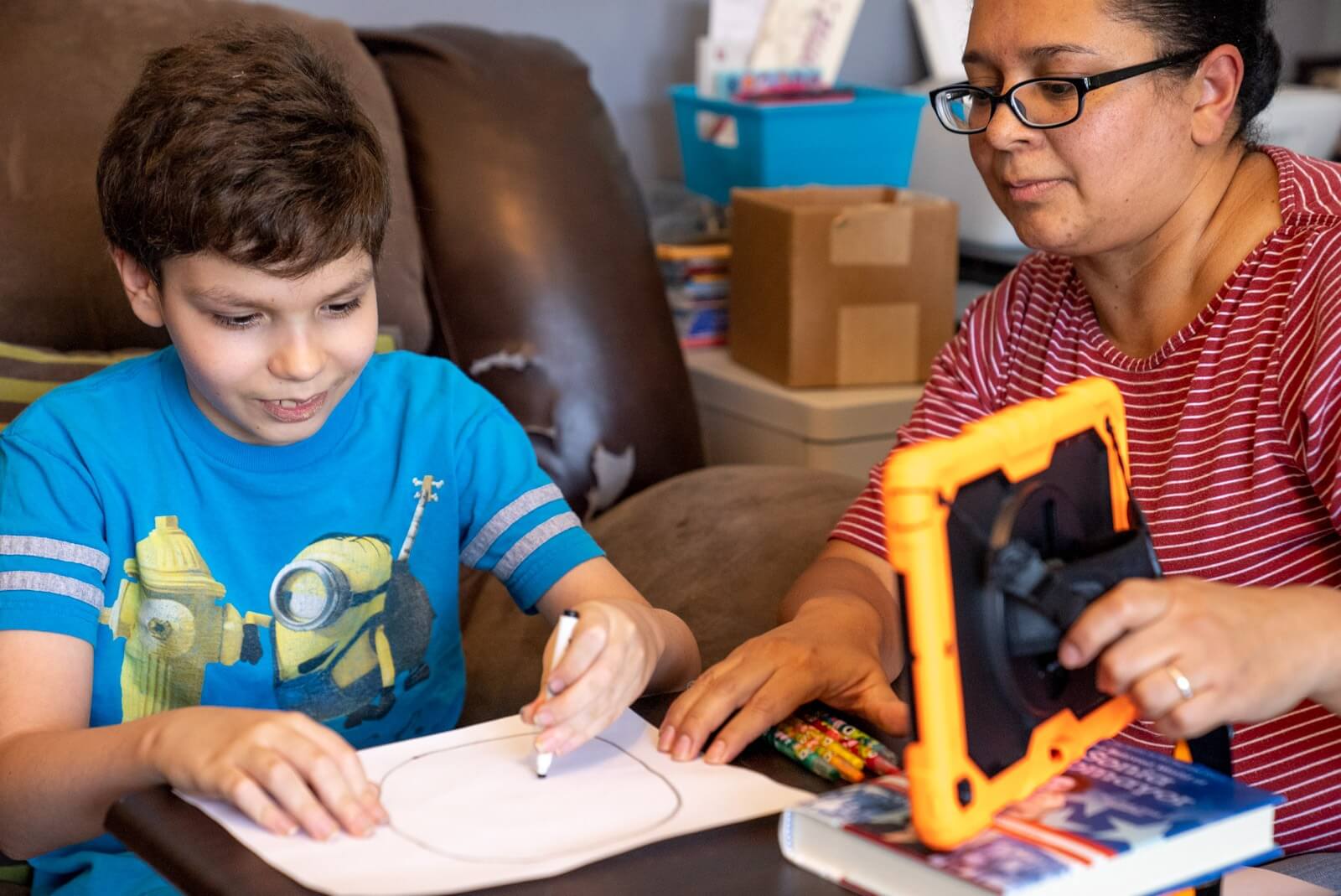 Therapist helping a boy trace a drawing beside a tablet