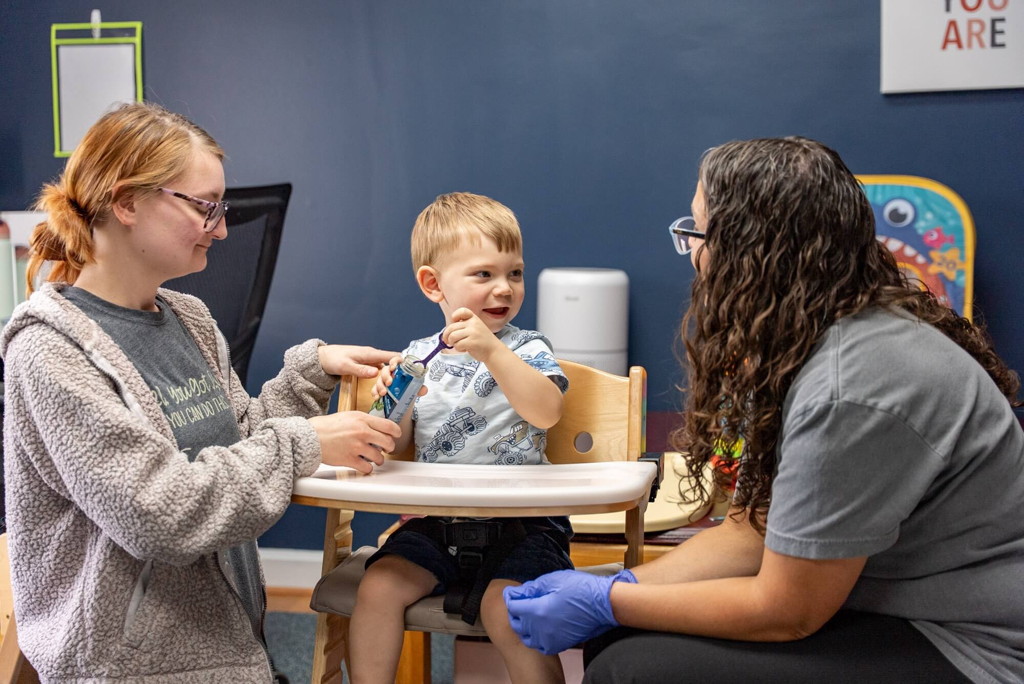 Toddler in a feeding chair with two therapists during a feeding session