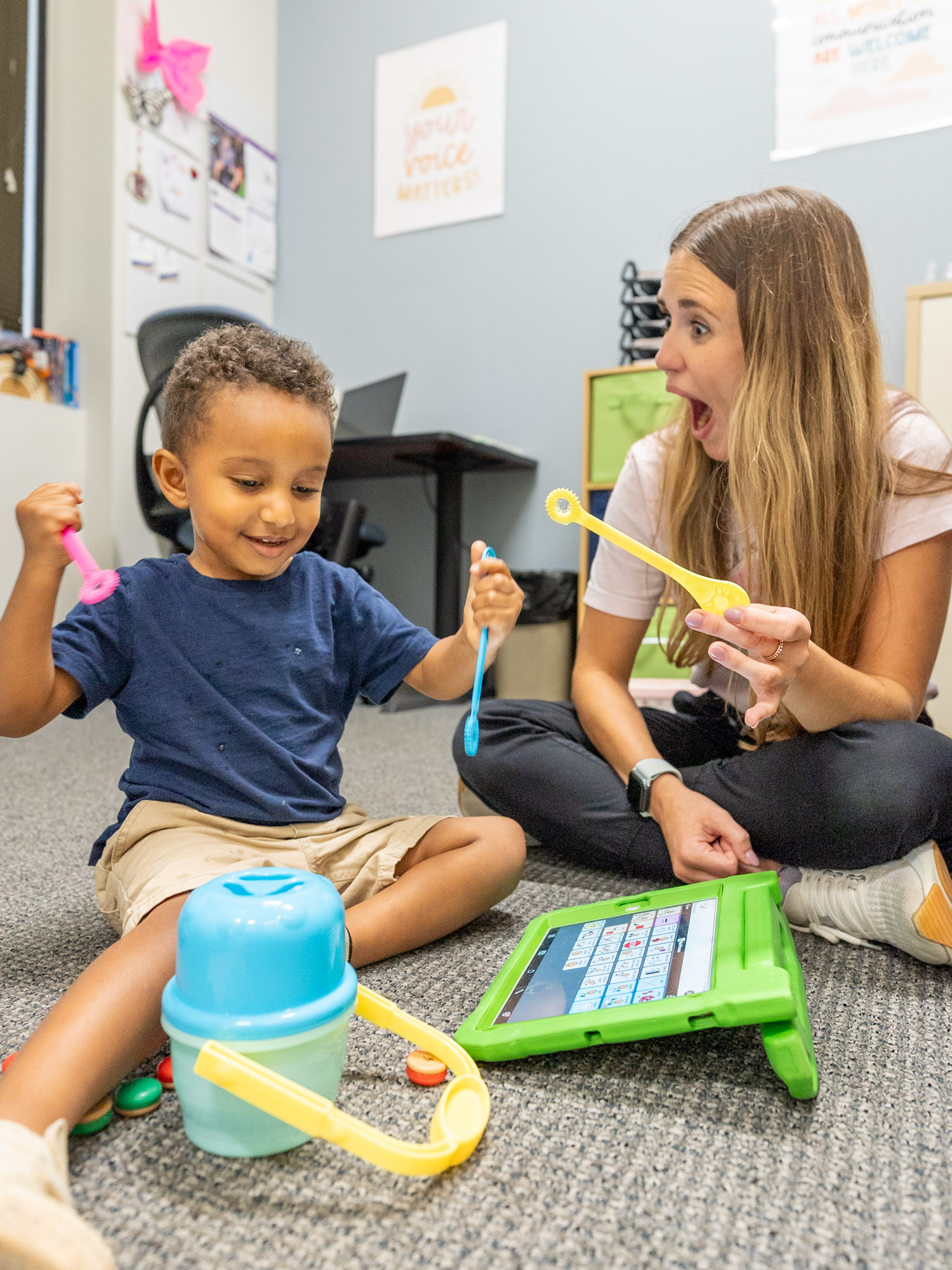 Therapist and child playing with toys and a tablet on the floor