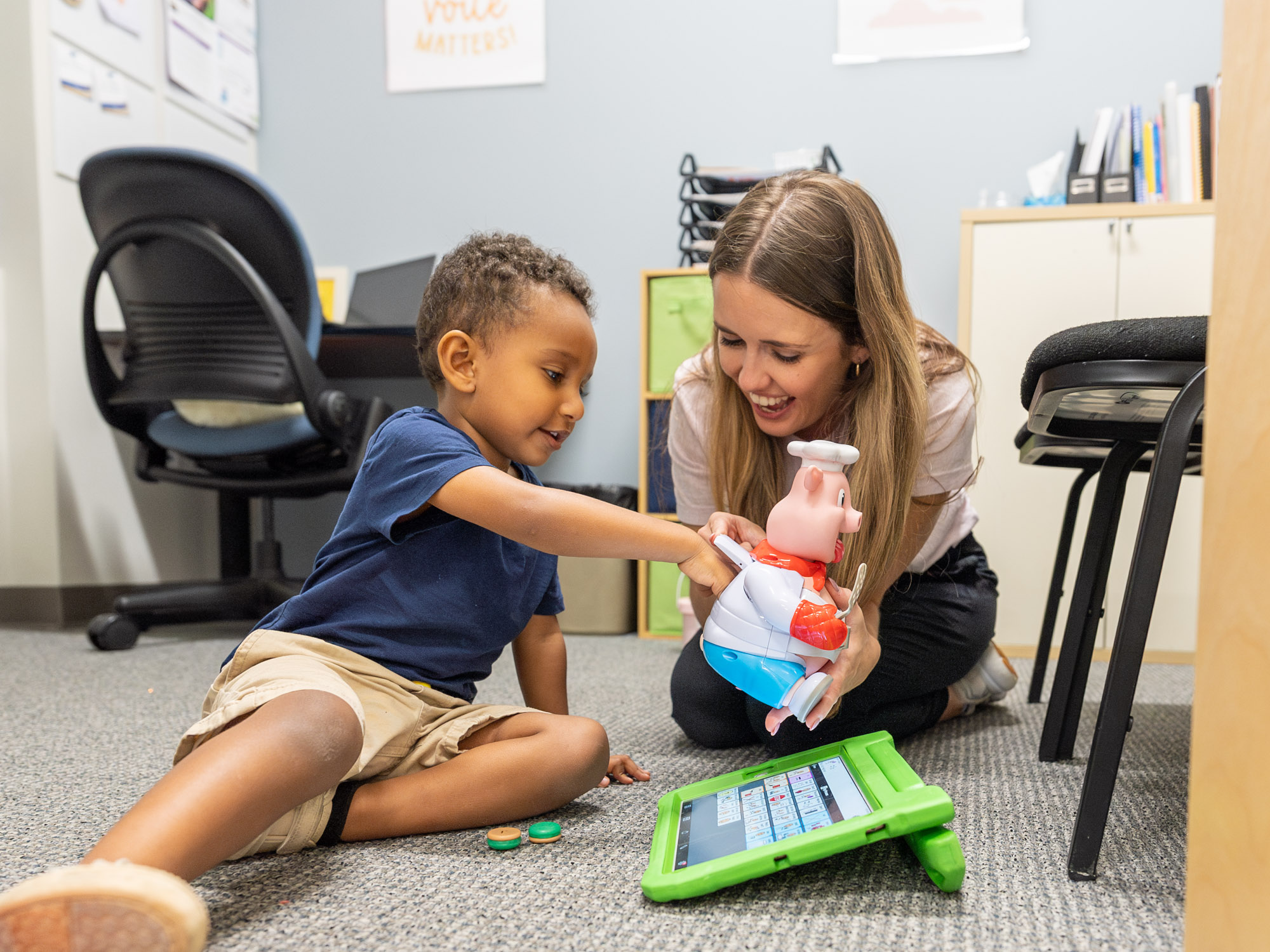 Therapist and child playing with a toy and a tablet on the floor