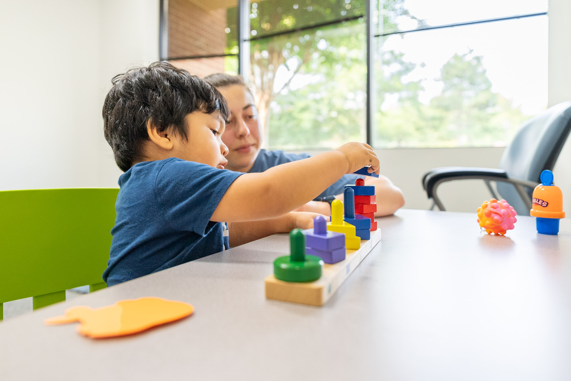 Child stacking shape pieces on a table with a therapist