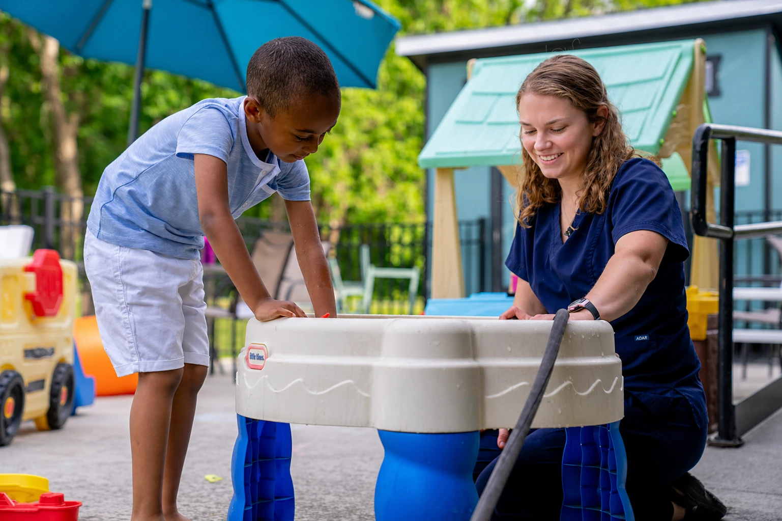 Therapist and child playing at an outdoor water table