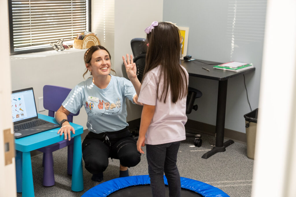 Therapist giving a high five to a young girl in a therapy room