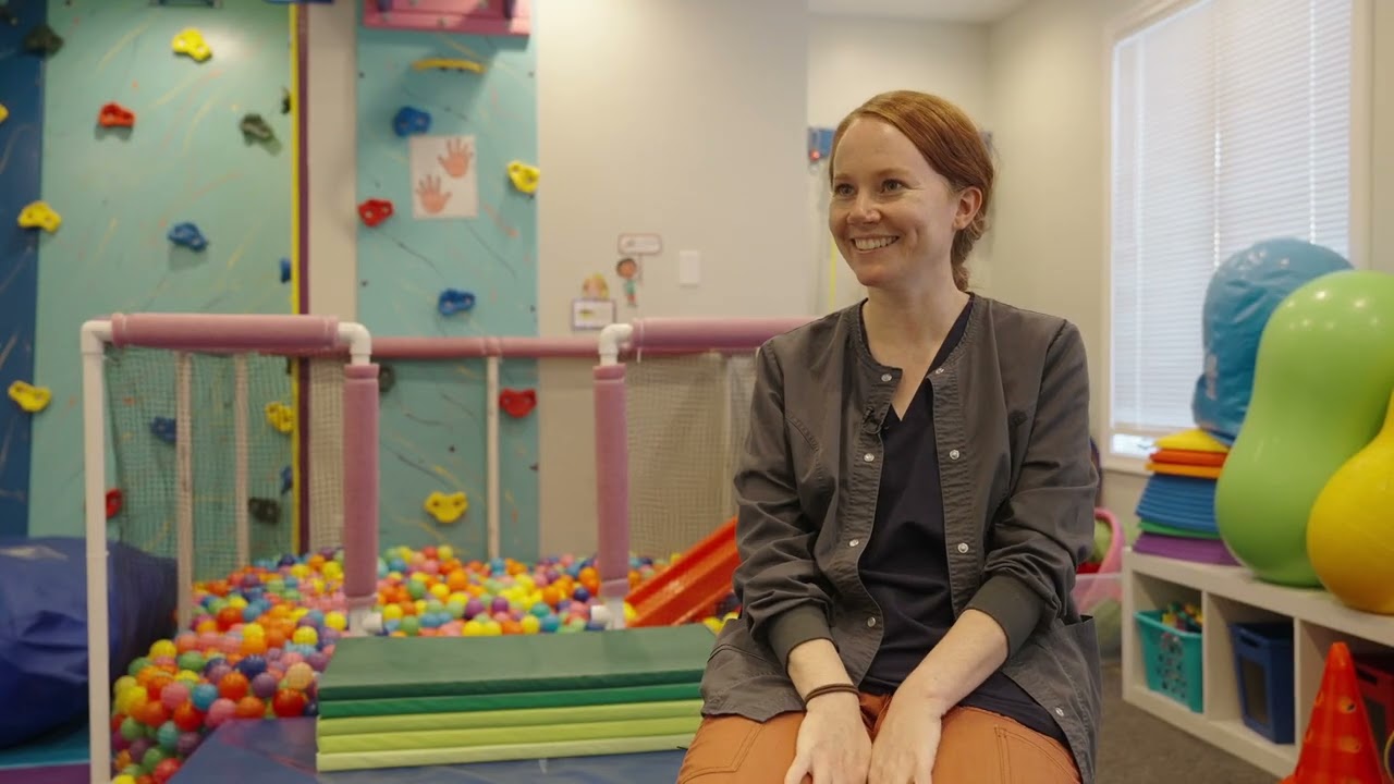 Therapist seated in a sensory gym with a climbing wall and ball pit