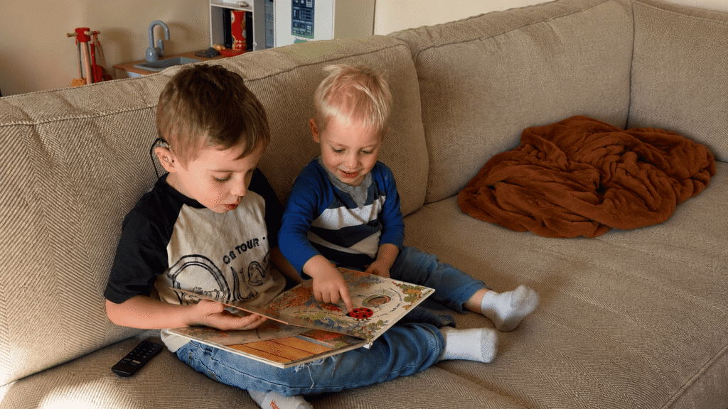 Two young boys reading a picture book together on a couch