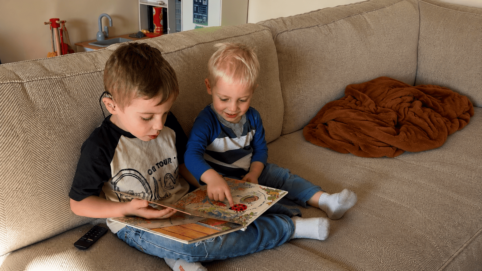 Two young boys reading a picture book together on a couch